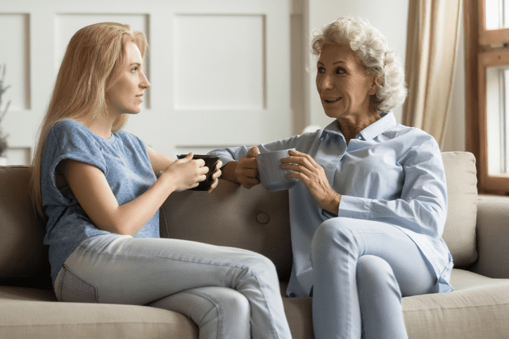 A mother and daughter holding coffee cups and sitting on a couch talking