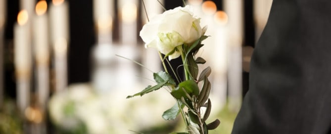 closeup of arms holding white rose with candles in the foreground