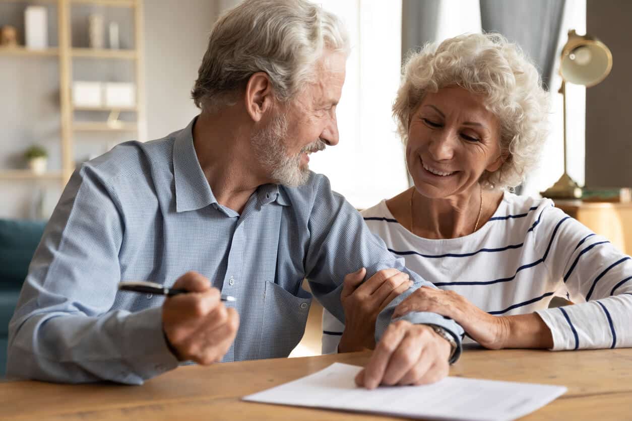 Compassionate Elderly Couple at Home Elderly couple smiling and holding hands, showing love and support in a cozy home setting.
