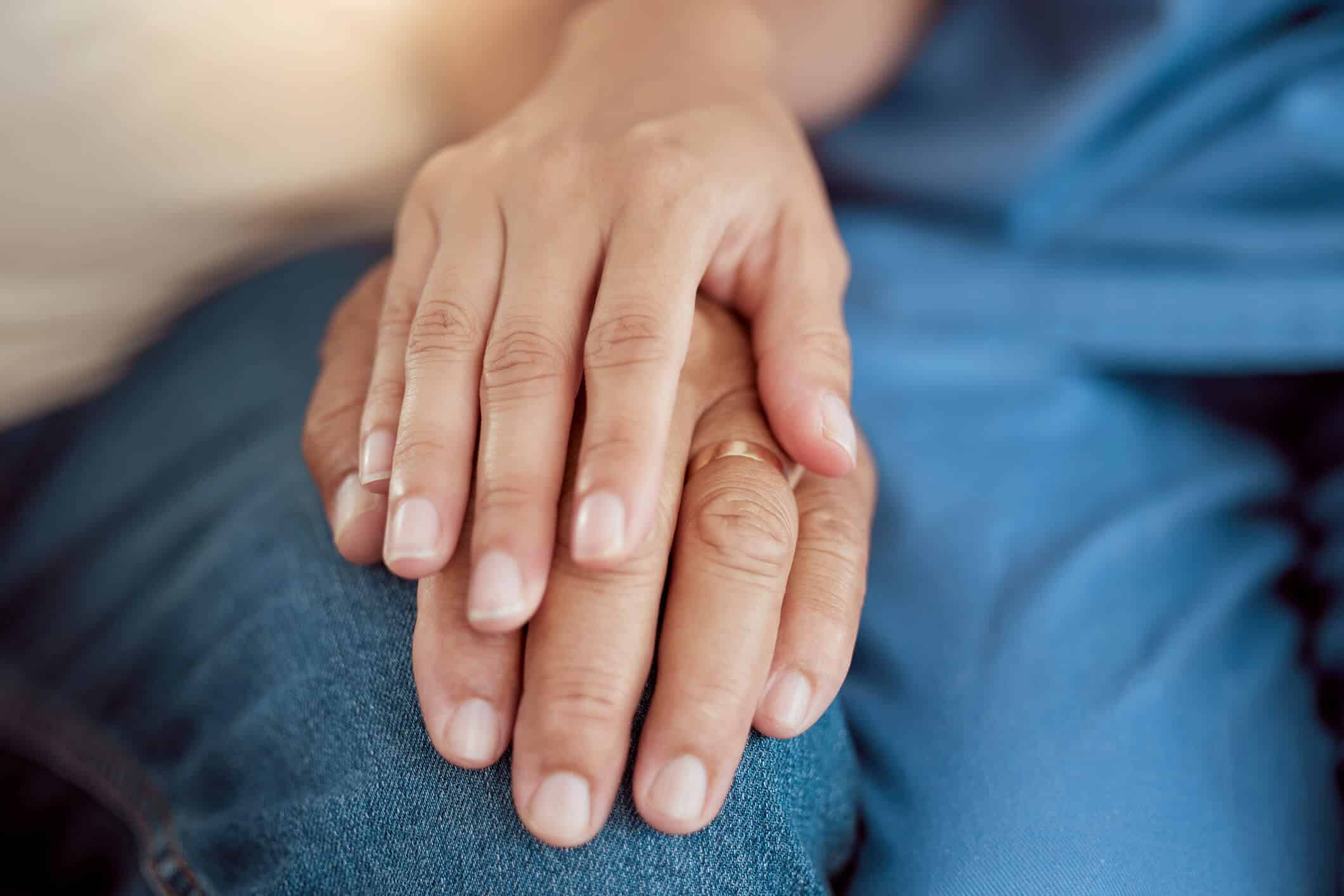 Compassionate Hand-Holding in Grief Close-up of two hands gently holding each other, symbolizing comfort and support during a difficult time.