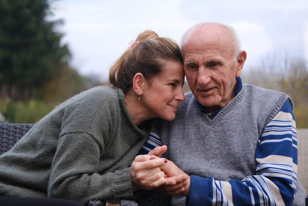 Tender moment between an elderly man and a middle-aged woman, reflecting on life choices and the dignified simplicity of cremation compared to traditional burial.