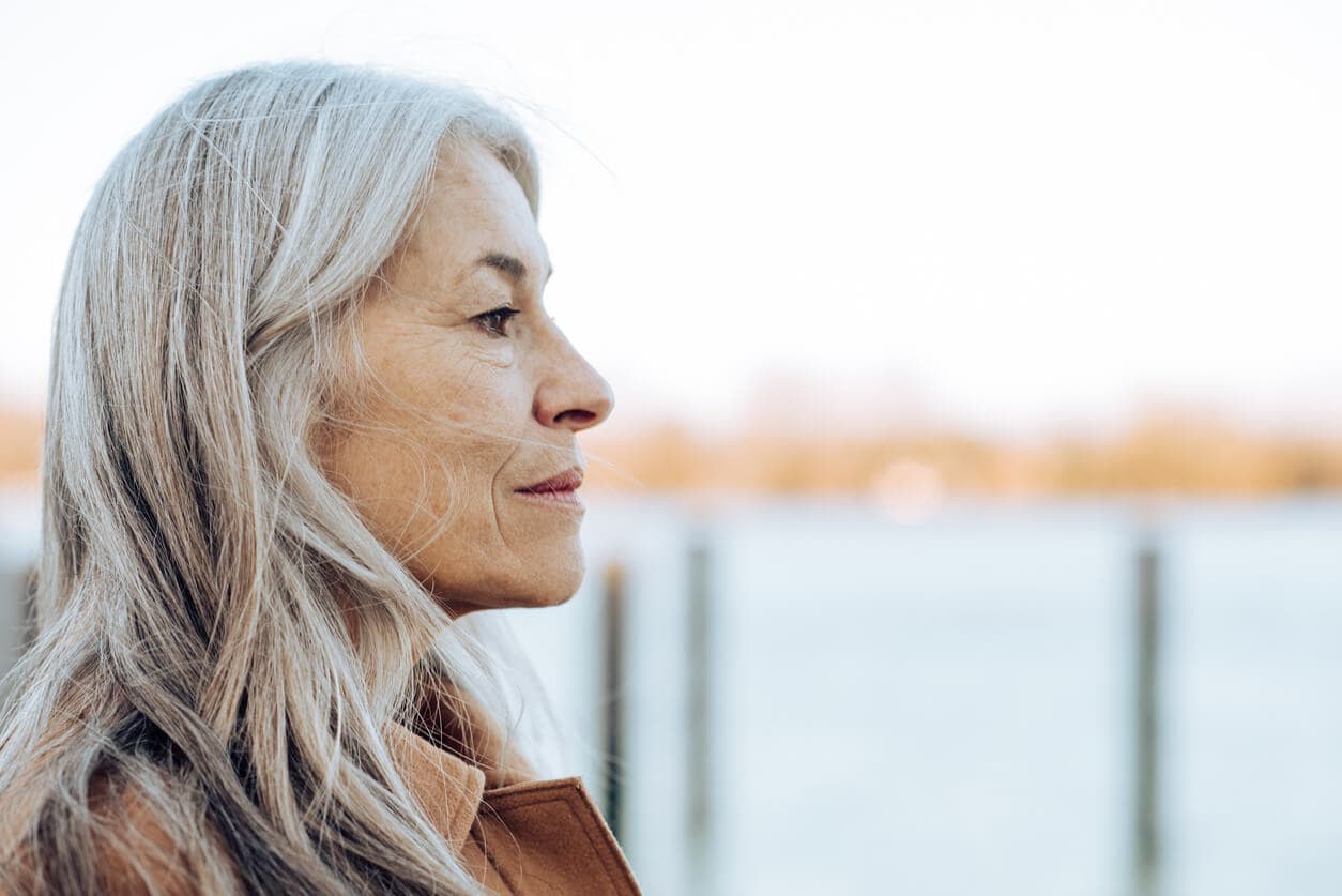 Contemplative senior woman overlooking a tranquil lake, representing the thoughtful consideration of cremation cost comparison.