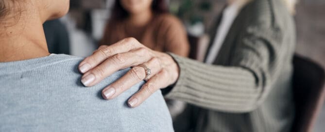 person puts hands on grieving person’s shoulder