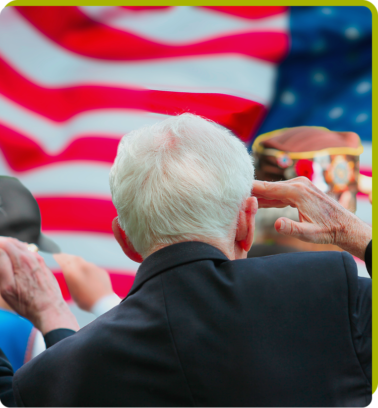 Elderly man saluting during a memorial event with an American flag in the background, honoring service members.